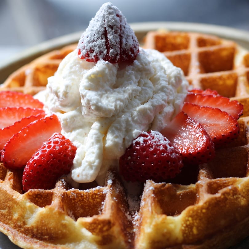 Golden waffle topped with whipped cream, fresh strawberries, and powdered sugar at Pinch Kitchen+Bar.