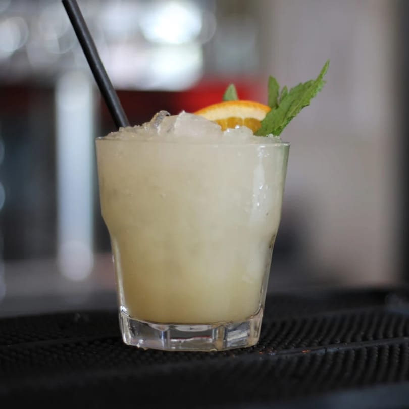 A Pinch Kitchen+Bar cocktail with crushed ice, orange slice, and mint garnish.