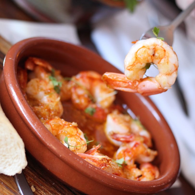 A fork lifts a succulent shrimp from a terracotta bowl of Pinch Kitchen+Bar's American-style shrimp scampi.