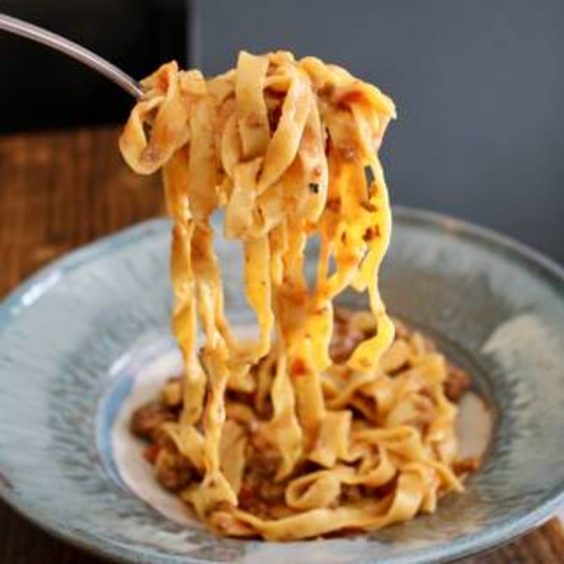 Fork lifting creamy fettuccine pasta with meat sauce from a blue bowl at Pinch Kitchen+Bar.