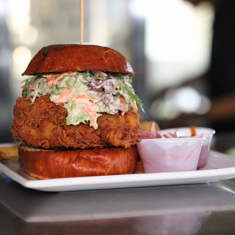 Crispy fried chicken sandwich with coleslaw on a brioche bun, served with pickled onions.